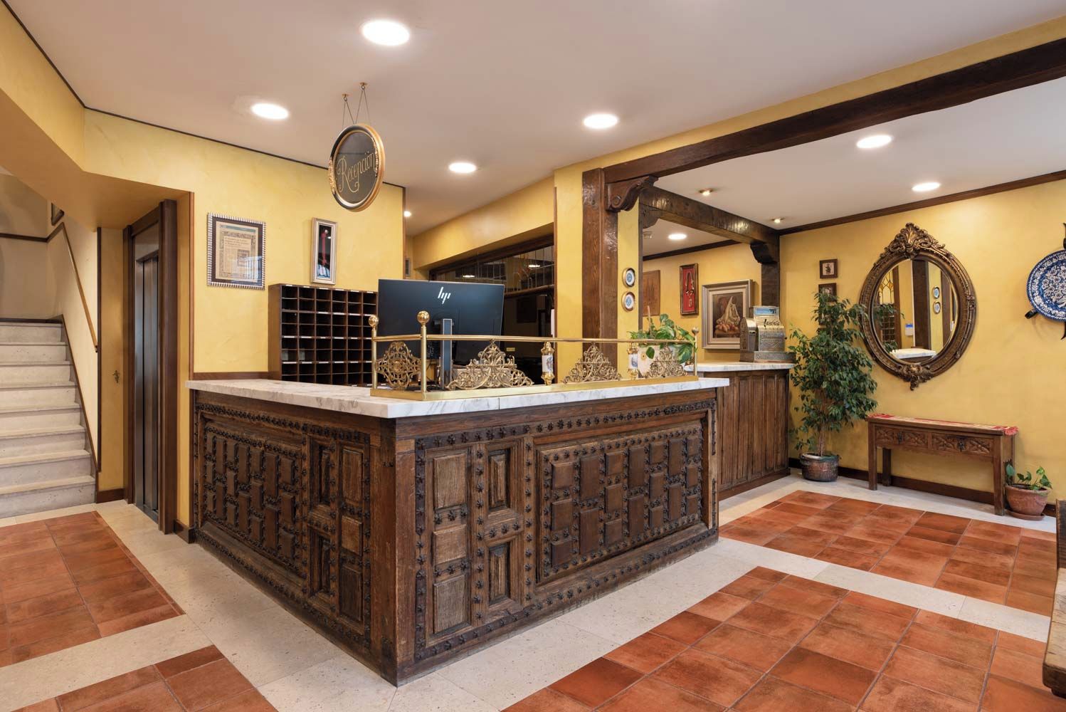 A reception area with a marble counter, a reception desk, a staircase, and a wall with a mirror and framed pictures.