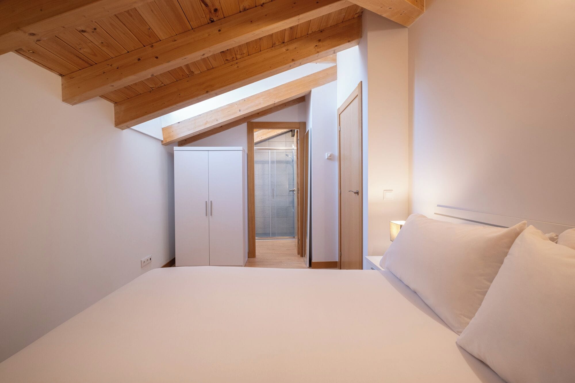 Een slaapkamer met een groot bed, houten plafond, inloopkast en een badkamer met glazen deur.