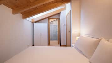 Een slaapkamer met een groot bed, houten plafond, inloopkast en een badkamer met glazen deur.
