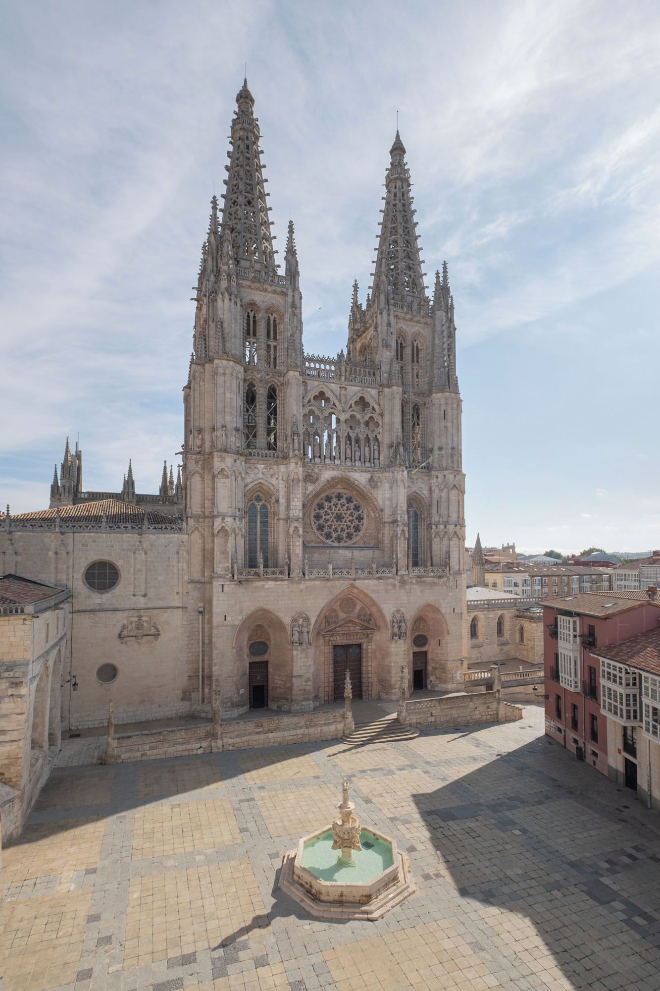 A cathedral with two tall spires, a large rose window, and a fountain in the courtyard.