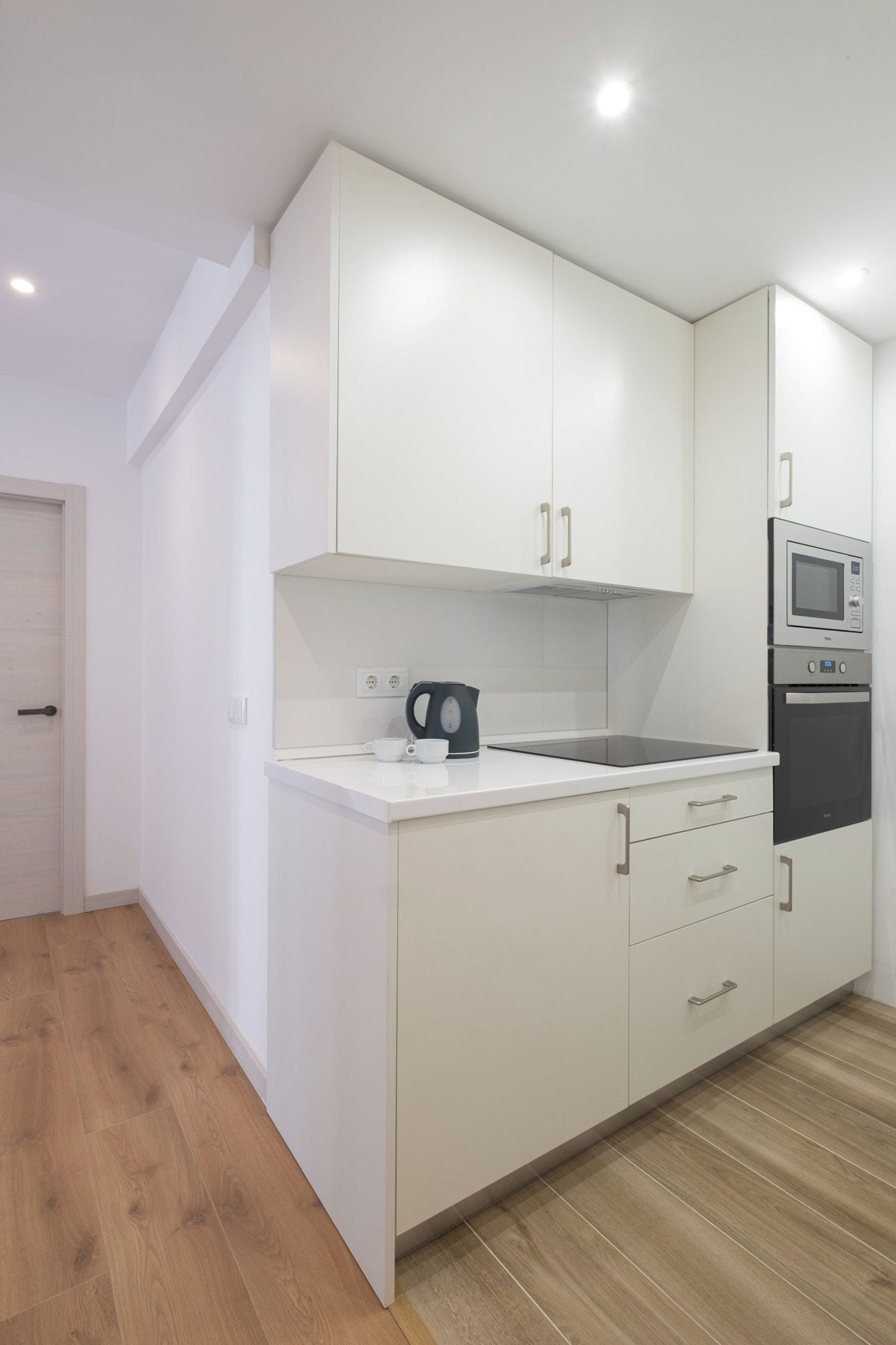 A modern kitchen with white cabinets, a microwave, and a kettle on the countertop.