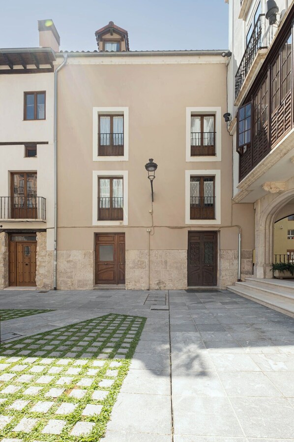 Un edificio con una entrada central, un pequeño patio con pavimento estampado y un farol.
