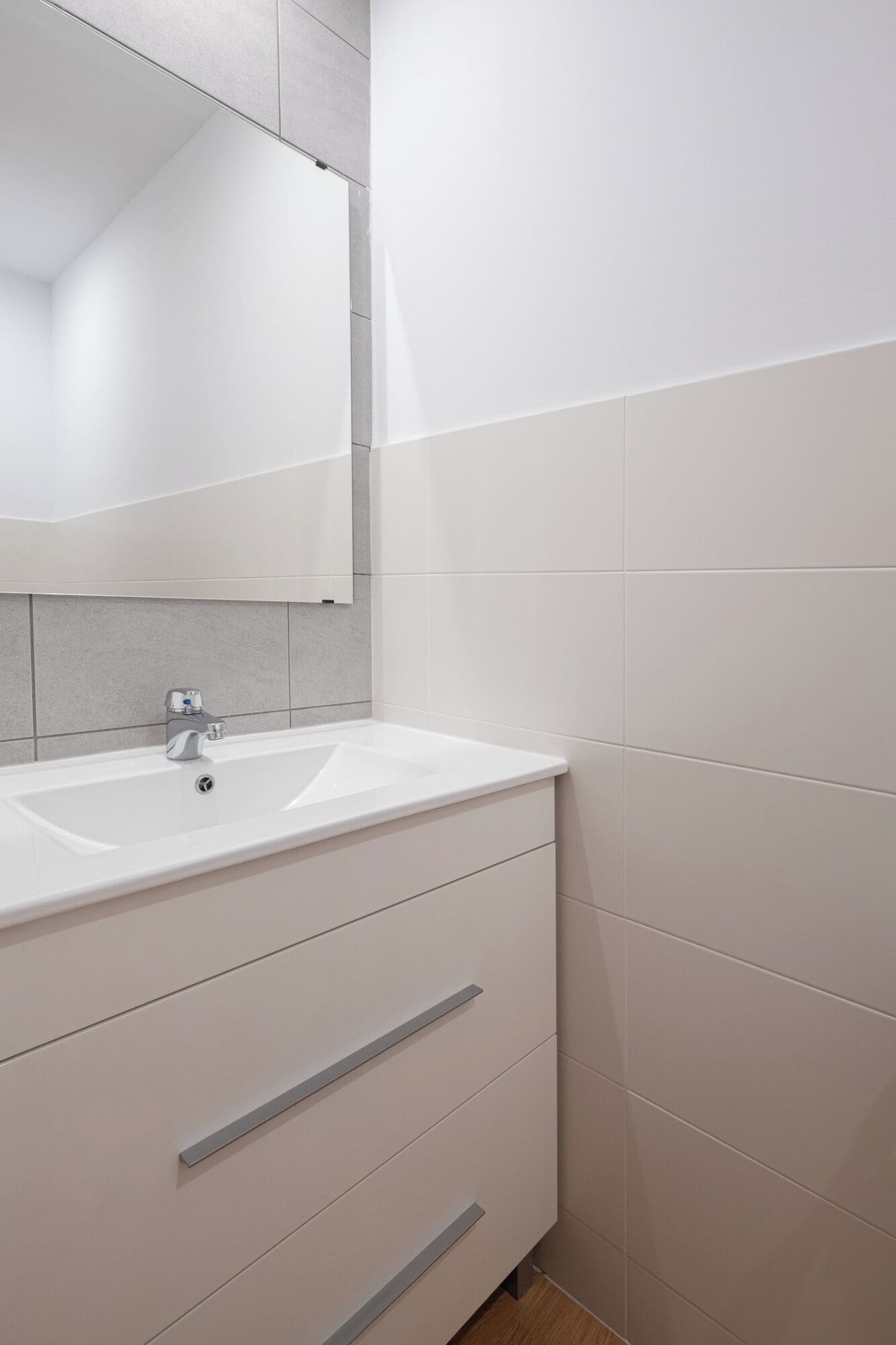 Een badkamer met een wit wastafel, een spiegel erboven en een betegelde muur.