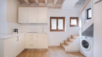A compact kitchen with wooden beams, a built-in washing machine, and a small window.