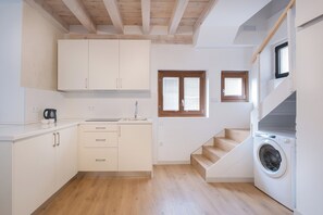 Una cocina compacta con vigas de madera, lavadora integrada y un ventanal pequeño.