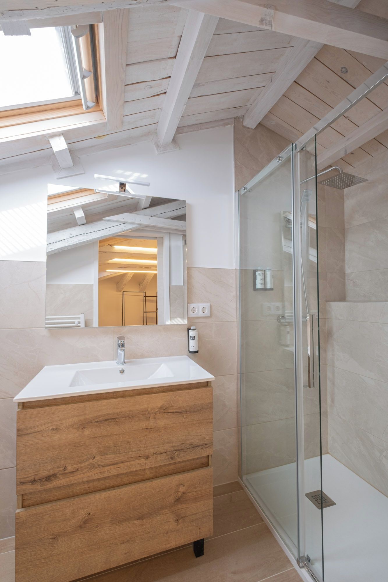Un baño moderno con tocador de madera, cabina de ducha de vidrio y tragaluz.