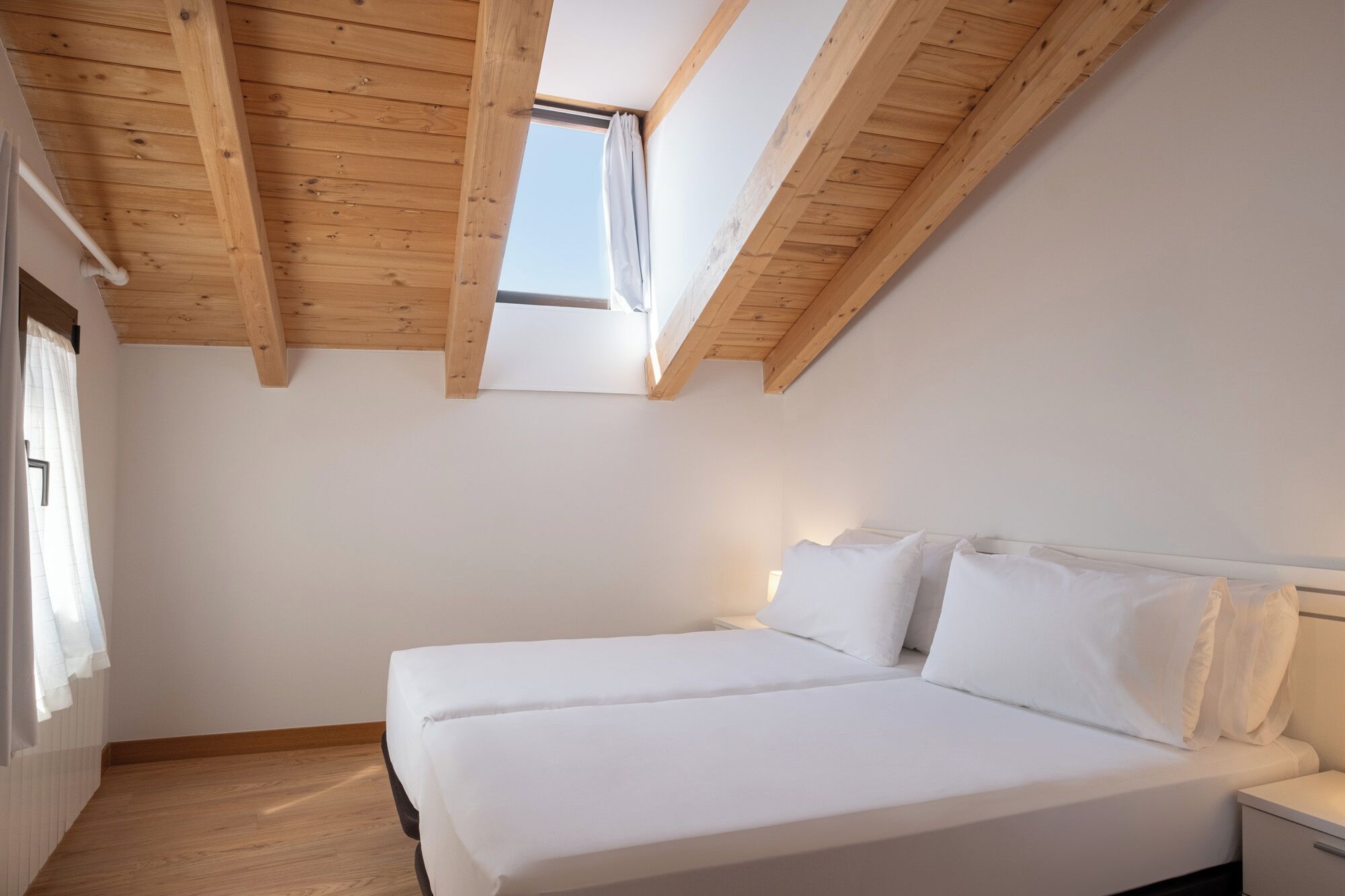 Ein Schlafzimmer mit geneigter Decke, einem Oberlicht und einem Bett mit weißer Bettwäsche.