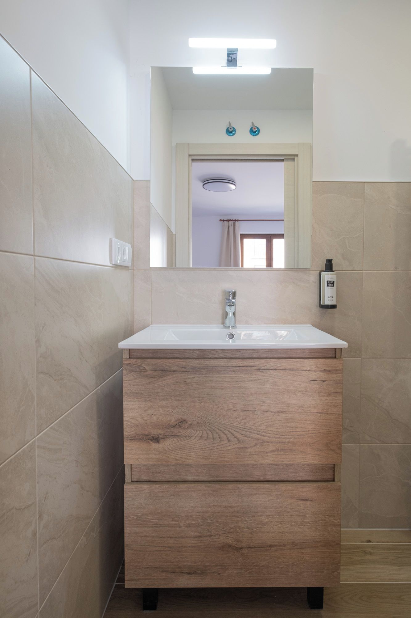 Un baño con tocador de madera, espejo y dispensador de desinfectante para manos.