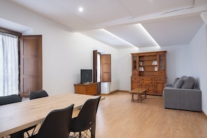 A modern living room with a wooden dining table, grey sofa, and a built-in wooden cabinet.