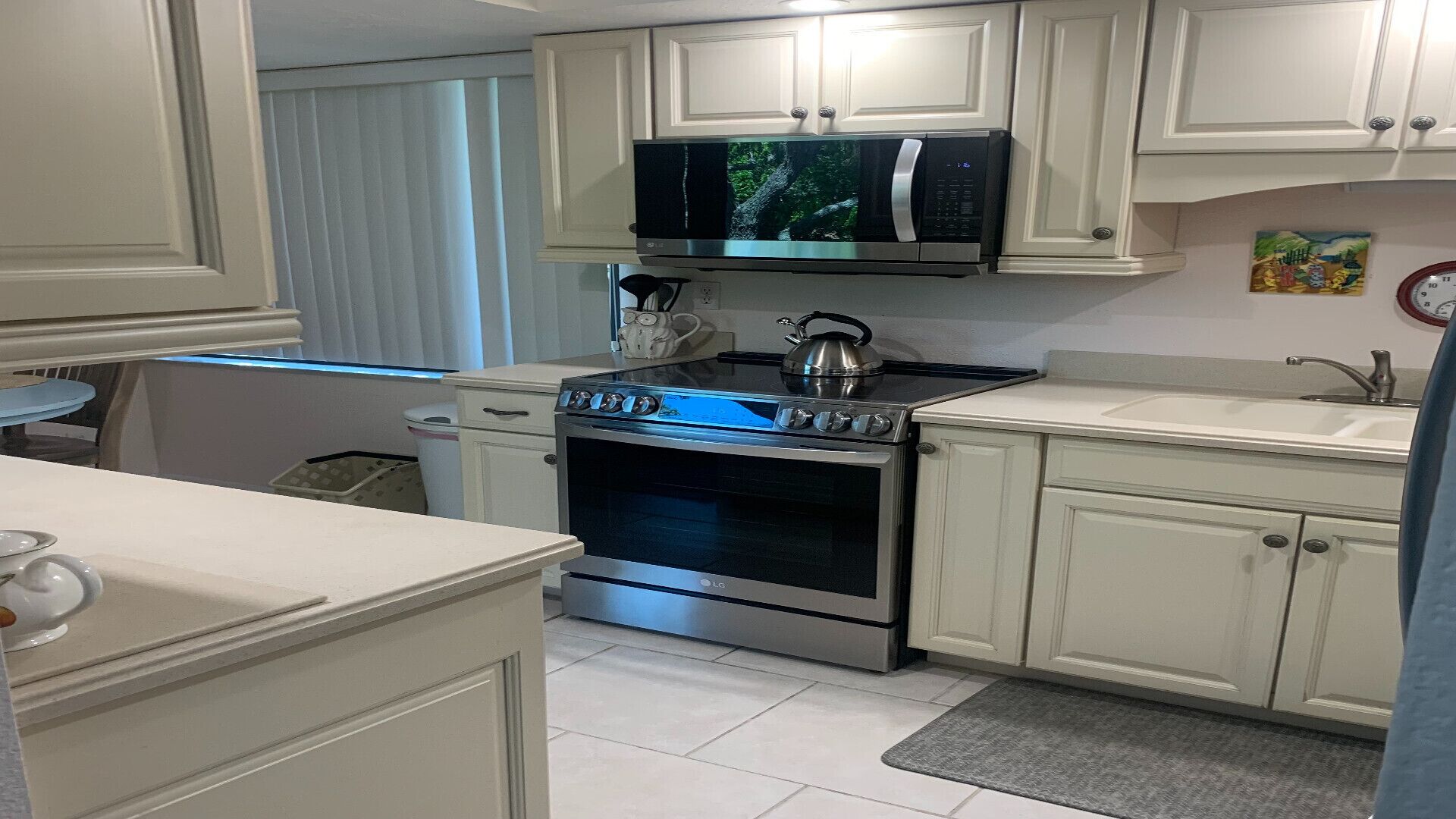 A kitchen with white cabinets, a microwave, an oven, and a kettle.