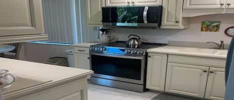 A kitchen with white cabinets, a microwave, an oven, and a kettle.