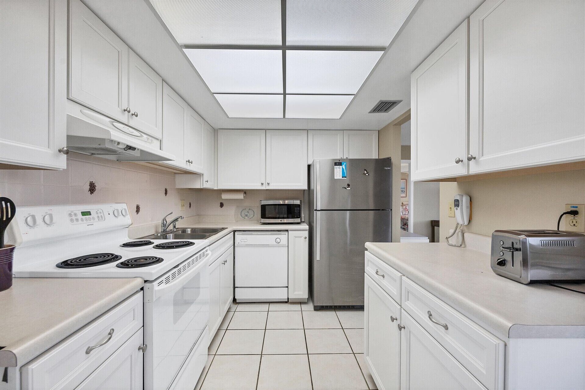 A modern kitchen with white cabinets, a stainless steel refrigerator, a microwave, and a stove.