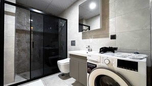 Une salle de bain moderne avec une douche à parois de verre, des toilettes, un lave-linge et un lavabo avec un miroir au-dessus.