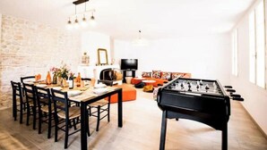 A dining area with a long table and chairs, a foosball table, a television, and a stone wall. - "Côté sauvage" 4-star vacation rental for 16 people (La Tremblade)