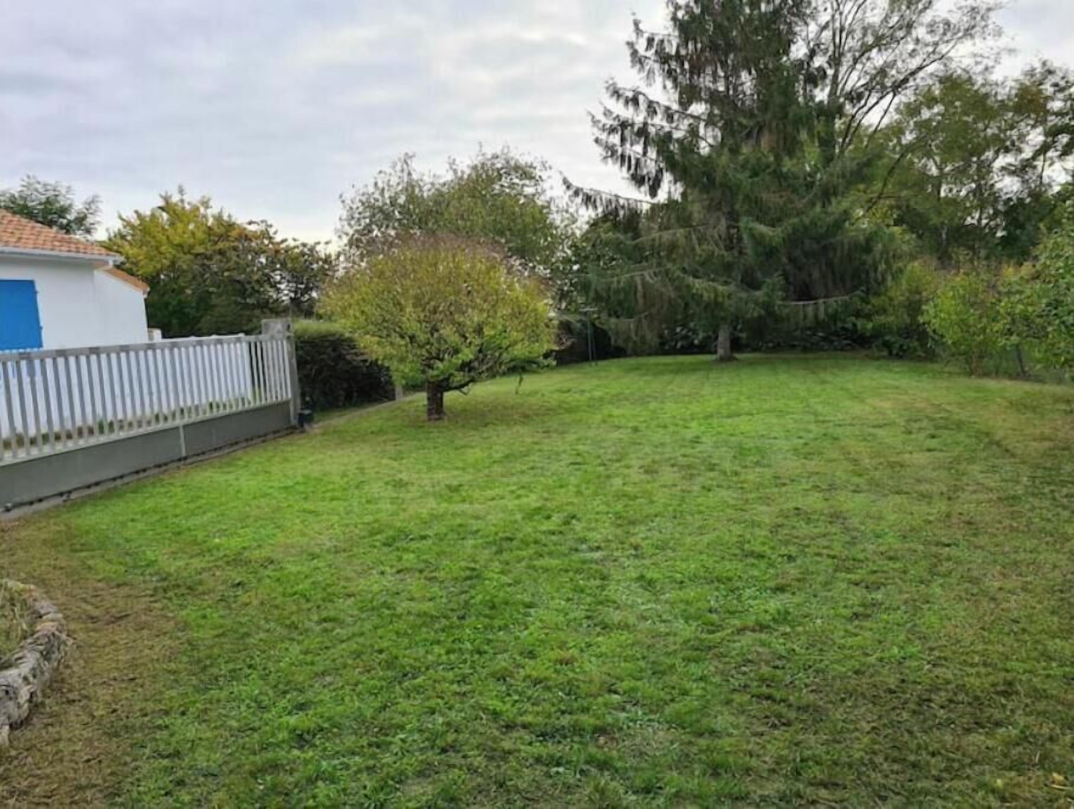 A grassy yard with a white fence, a small tree, and a building with a blue door.