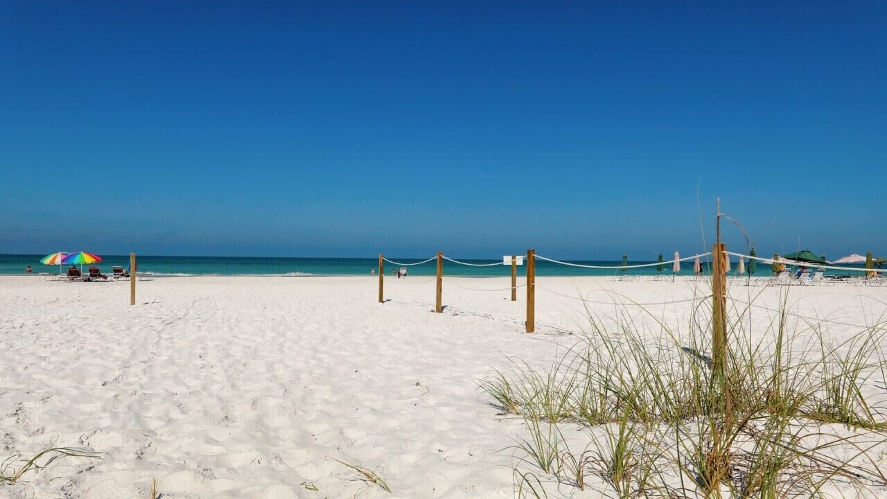 A beach with a volleyball net, a few umbrellas, and a clear sky.