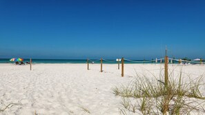 Ein Strand mit Volleyballnetz, einigen Sonnenschirmen und blauem Himmel.