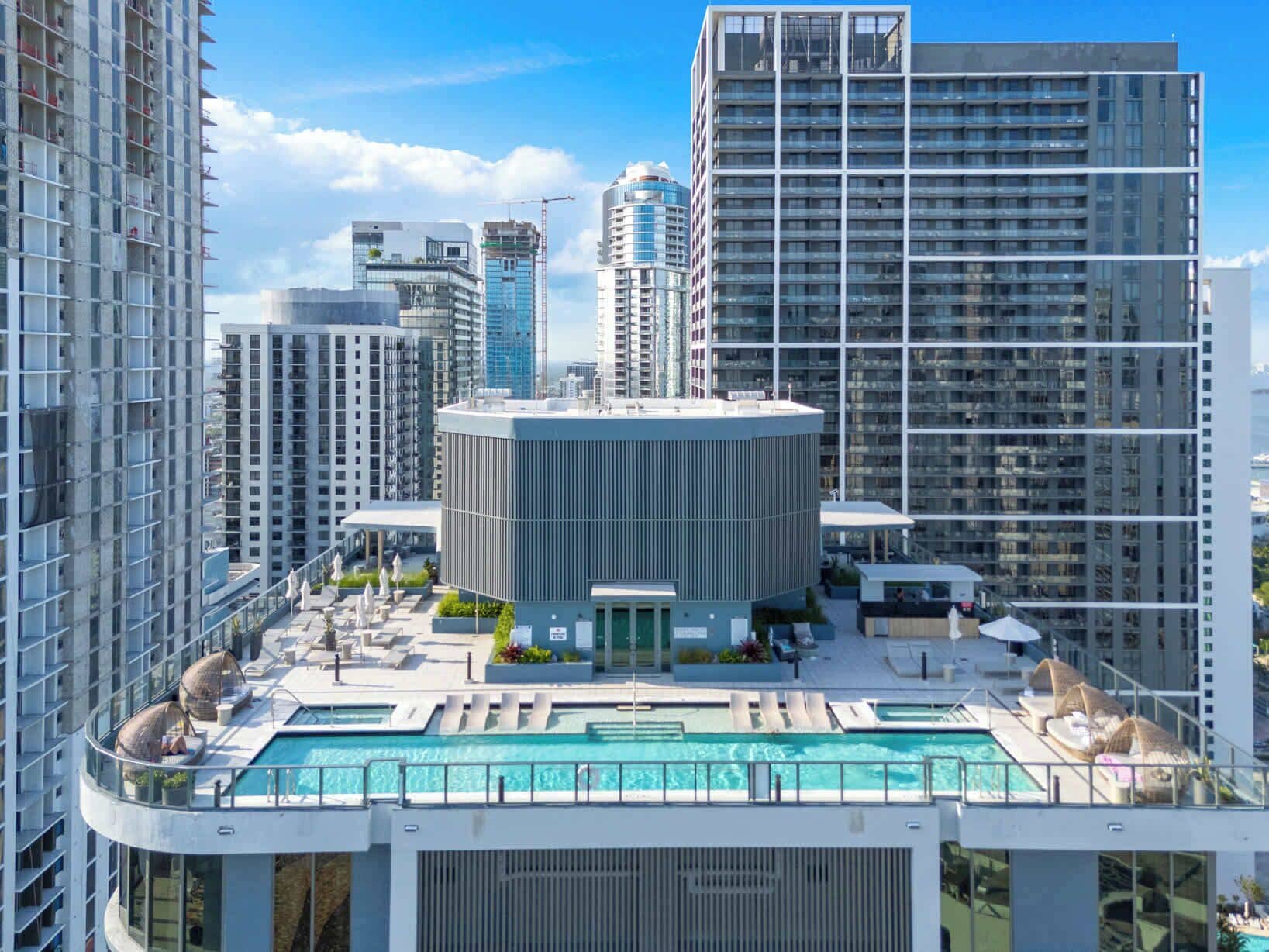A high-rise building with a rooftop pool and lounge area, surrounded by other tall buildings.