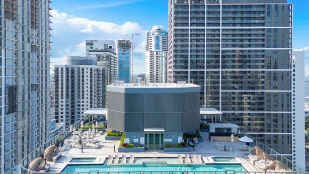 Um edifício alto com piscina e área de estar no terraço, rodeado por outros edifícios altos.
