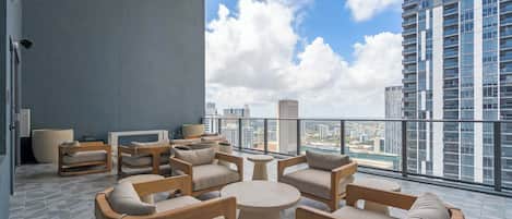 A modern outdoor seating area with multiple chairs and tables, a large potted plant, and a city view.