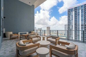Ein moderner Außenbereich mit mehreren Stühlen und Tischen, einer großen Pflanze im Topf und Blick auf die Stadt.