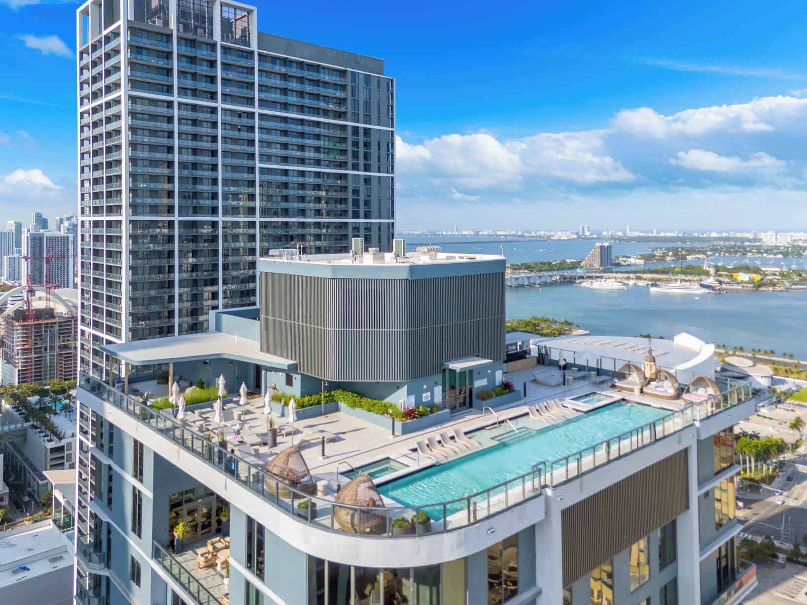 Un hotel moderno con piscina en la azotea, vistas al horizonte de la ciudad y una masa de agua al fondo.