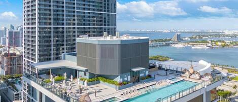 Un hotel moderno con piscina en la azotea, vistas al horizonte de la ciudad y una masa de agua al fondo.