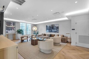 Ein modernes Wohnzimmer mit einer Sofagarnitur, Couchtisch und Sesseln. Große Fenster sorgen für natürliches Licht und bieten Blick auf die Stadtlandschaft.