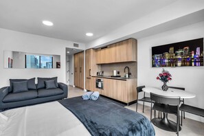 Ein modernes Hotelzimmer mit Bett, einer Sitzecke, einer Küchenzeile, einem Essbereich und Blick auf die Stadt.
