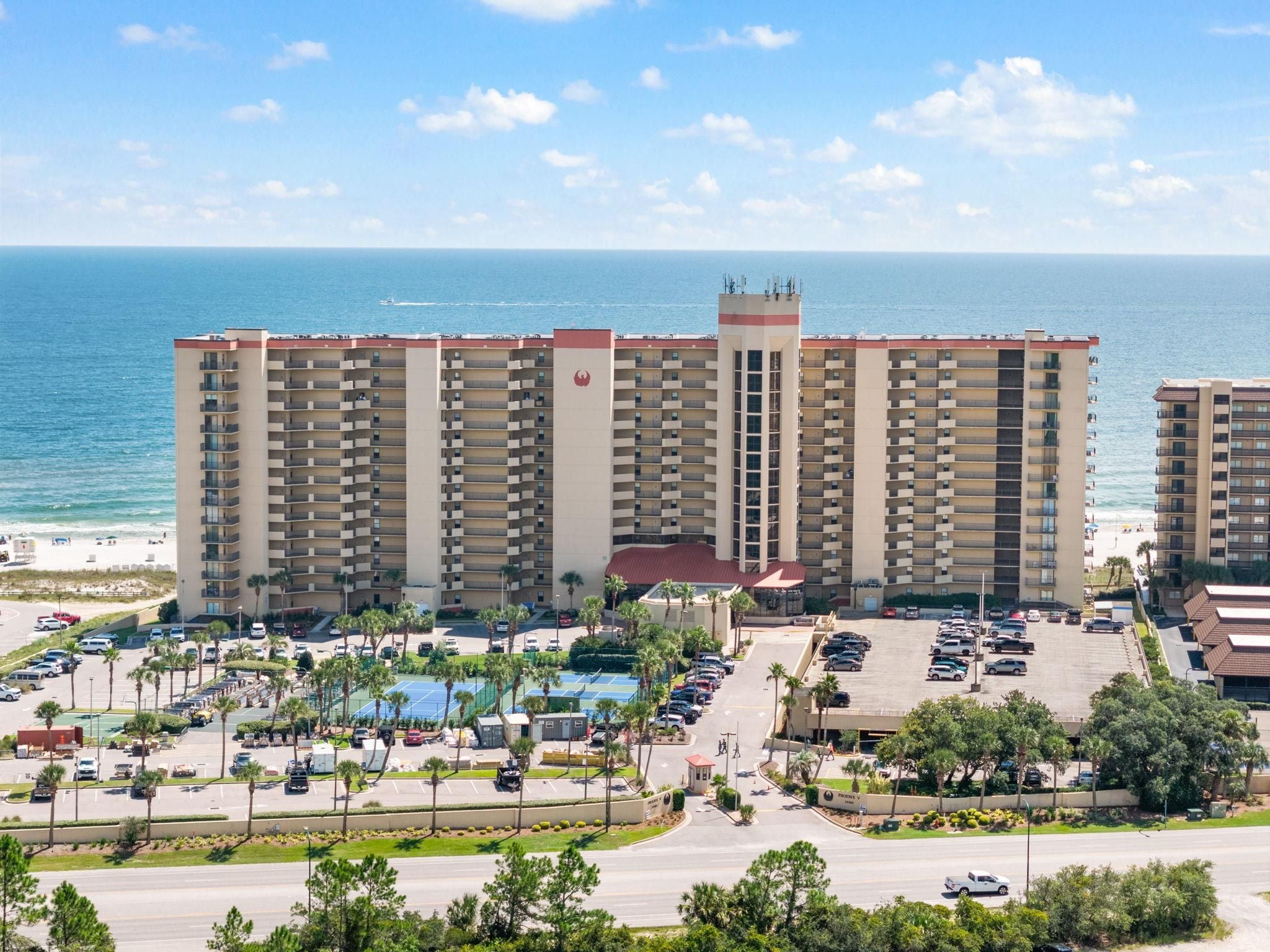 Hotel com vários andares, área de piscina, estacionamento e vista para o oceano.