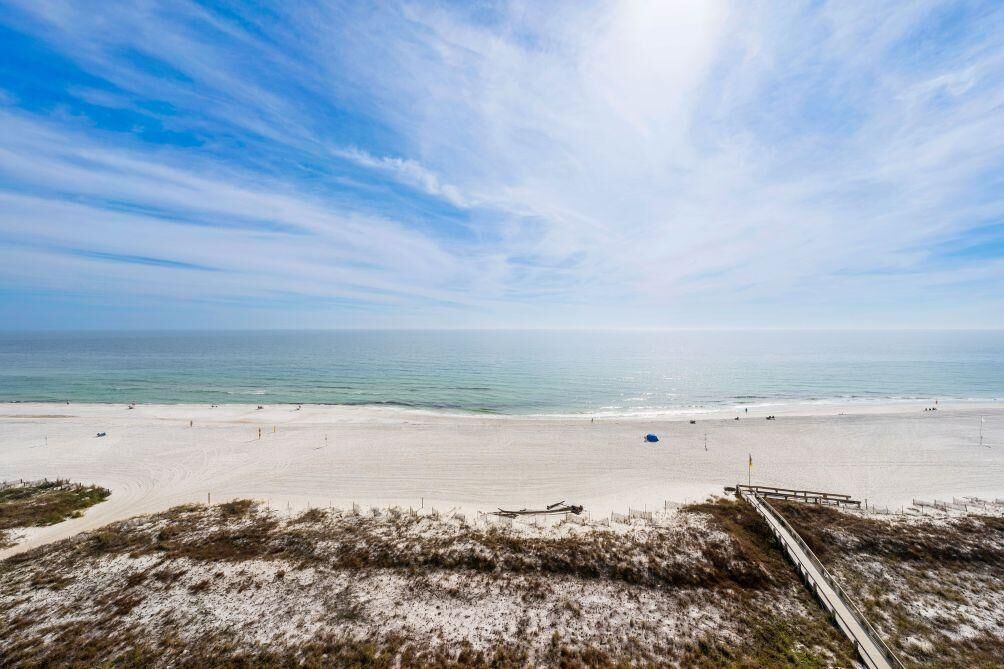 Ein Strand mit blauem Himmel, sandigem Ufer und einer hölzernen Promenade, die zum Wasser führt.