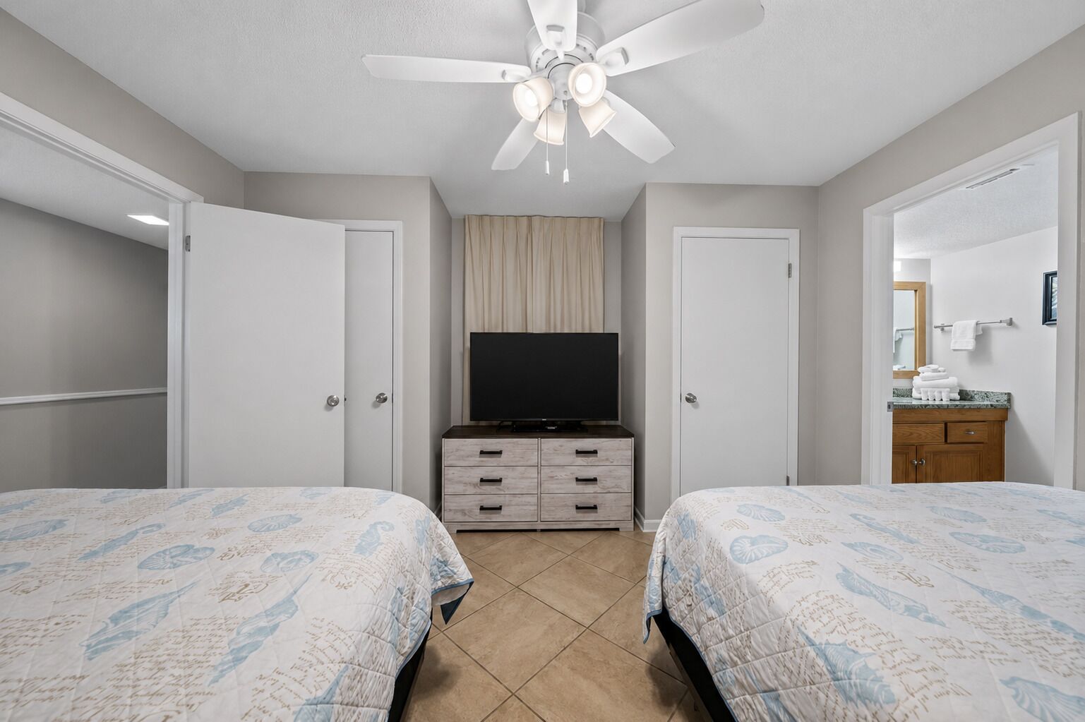A bedroom with two beds, a television, a ceiling fan, and a bathroom with a mirror and towel rack.