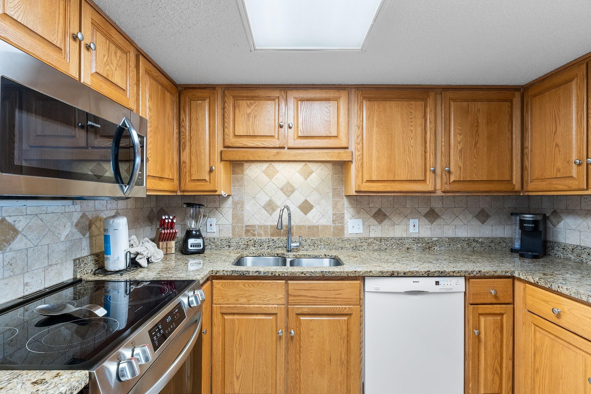 Una cocina moderna con armarios de madera, un microondas de acero inoxidable, un lavavajillas Bosch y una encimera de granito.