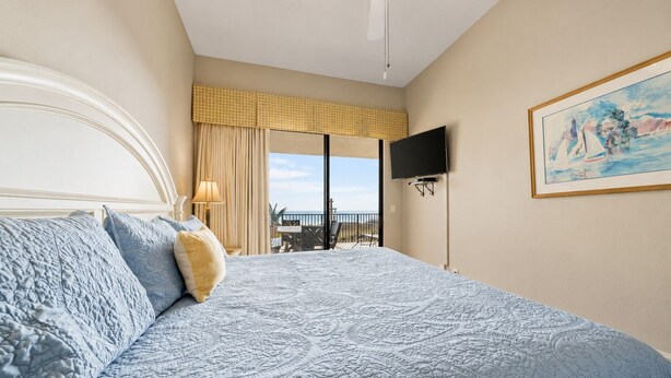 Ein Hotelzimmer mit einem großen Bett, einem Fernseher, einem Gemälde und Blick ins Freie.