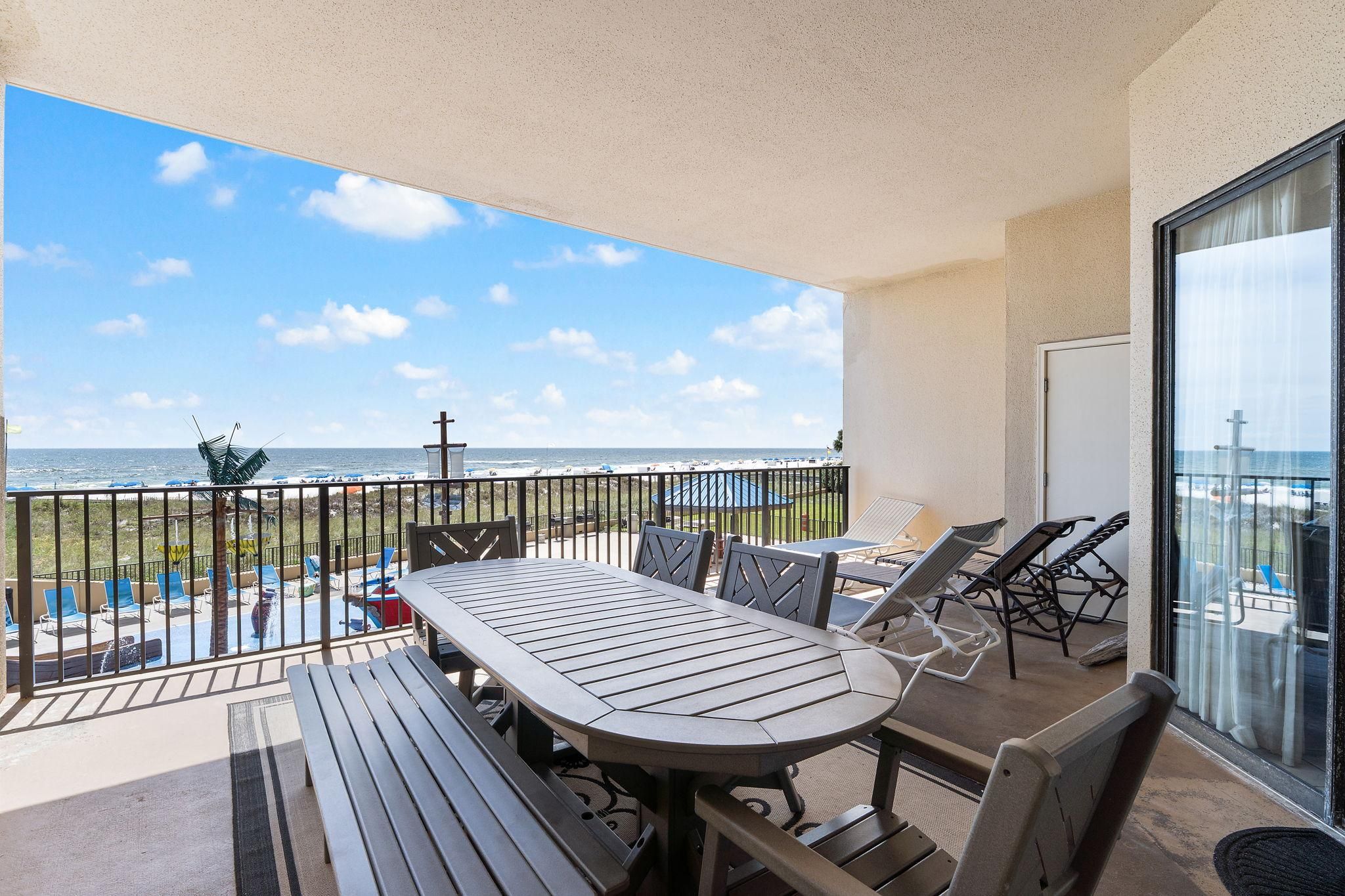 Un balcon avec une table et des chaises, donnant sur une piscine et l’océan.