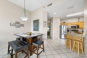 A kitchen with a dining area, featuring a wooden table, bar stools, and modern appliances. - Phoenix 5 106 (Orange Beach)