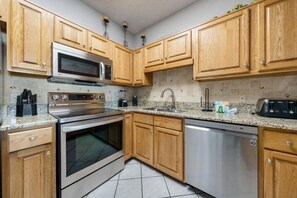 A kitchen with wooden cabinets, stainless steel appliances, granite countertops, and a dishwasher. - Phoenix 5 106 (Orange Beach)