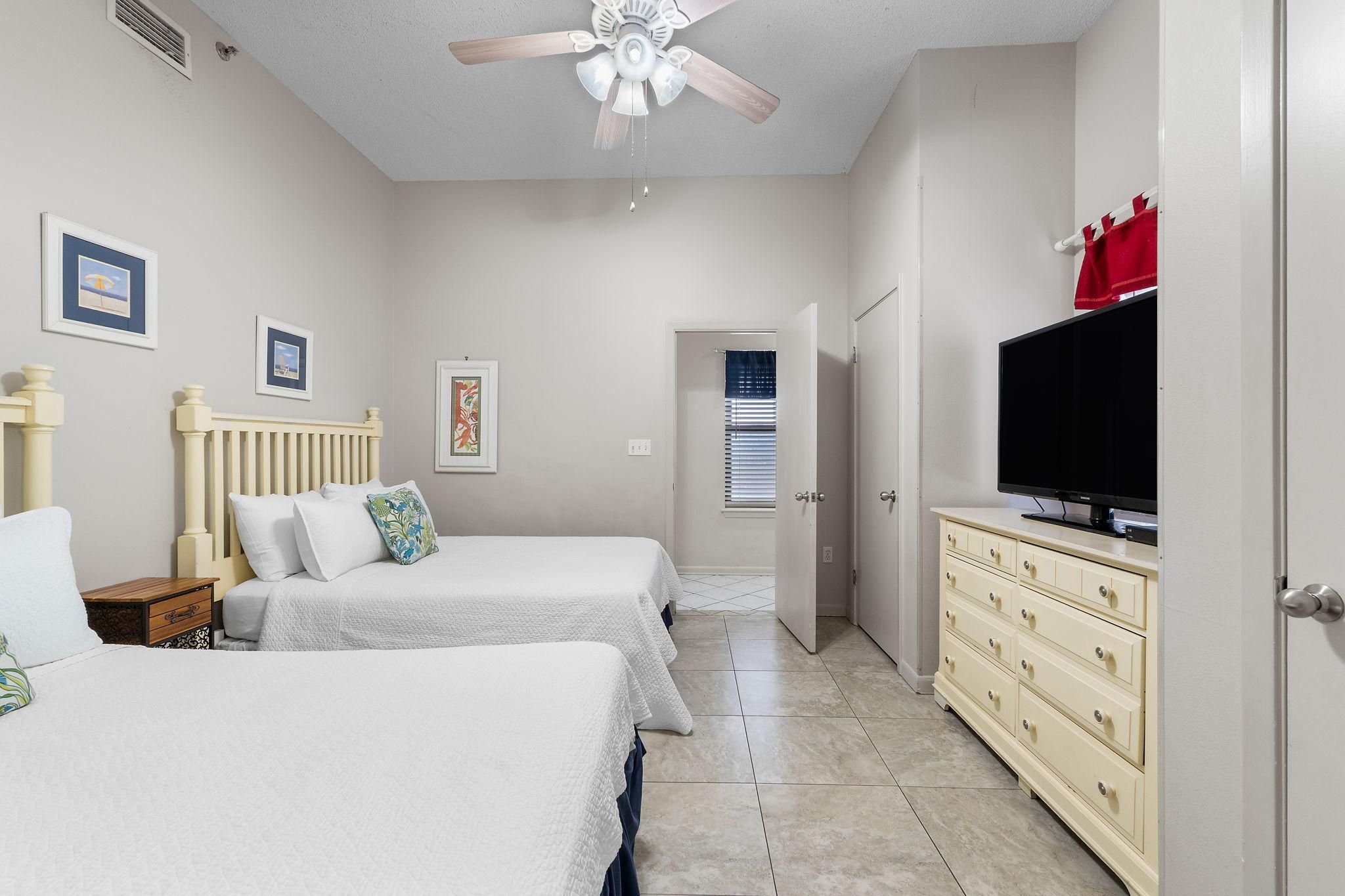 Une chambre avec deux lits, un ventilateur de plafond, une télévision et une commode.