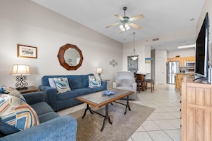 A modern living room with a blue sofa, a coffee table, and a dining area with a chair and table. - Phoenix 5 106 (Orange Beach)