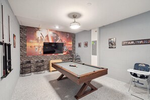 Ein Zimmer mit Billardtisch, einem an einer Ziegelwand montierten Fernseher und Deko im Star Wars-Design.