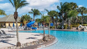 A pool area with a water slide, lounge chairs, and palm trees. - Paradise Palms Resort 103 (Orlando)