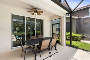 An outdoor patio with a table and chairs, a ceiling fan, and large windows offering views of the surrounding area. - Paradise Palms Resort 103 (Orlando)