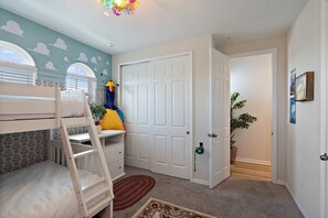 Ein Kinderzimmer mit Etagenbett, einer Tür, einem Blumentopf und einer Wand mit Wolkenmotiven.