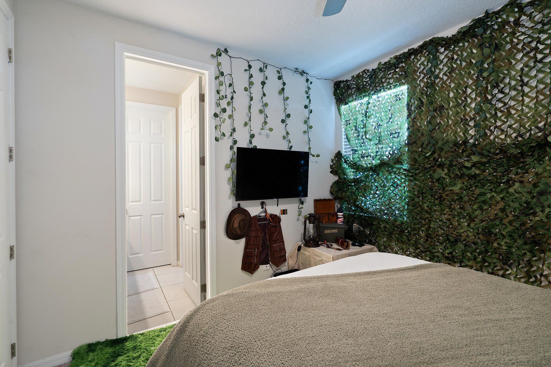 A bedroom with a bed, a television, and a wall covered in green foliage.