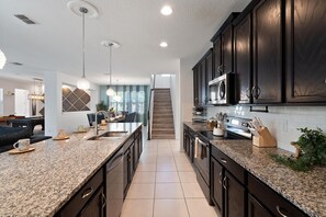 A modern kitchen with dark wood cabinets, granite countertops, and stainless steel appliances. - Solara Resort 330 - Nine Bedroom Villa, Sleeps 22 (Orlando)