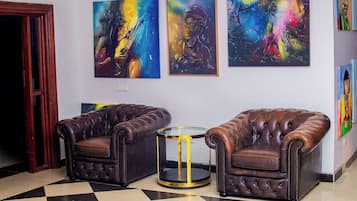 A room with two leather armchairs, a small round table, and three abstract paintings on the wall.