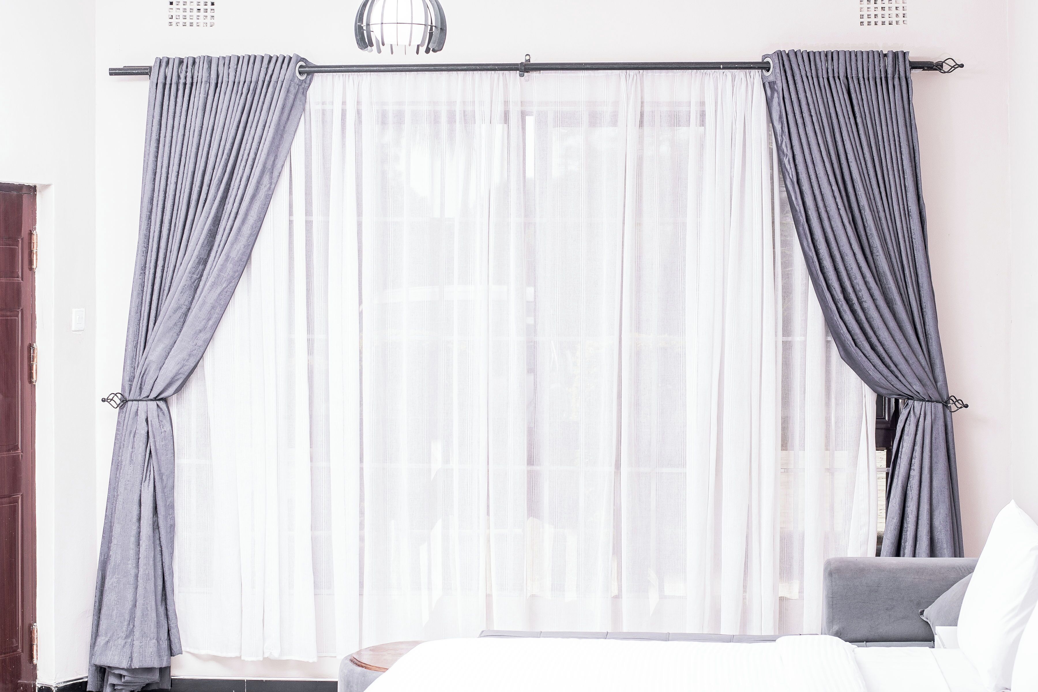Ein Hotelzimmer mit Bett, Stuhl und einem Fenster mit leichtem Vorhang.