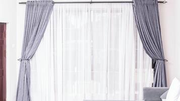 Ein Hotelzimmer mit Bett, Stuhl und einem Fenster mit leichtem Vorhang.