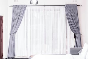 A hotel room with a bed, a chair, and a window with sheer curtains.