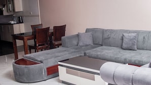 A modern living room with a grey sectional sofa, a matching ottoman, and a coffee table. - JALITHS Boutique Hotel (Lusaka)